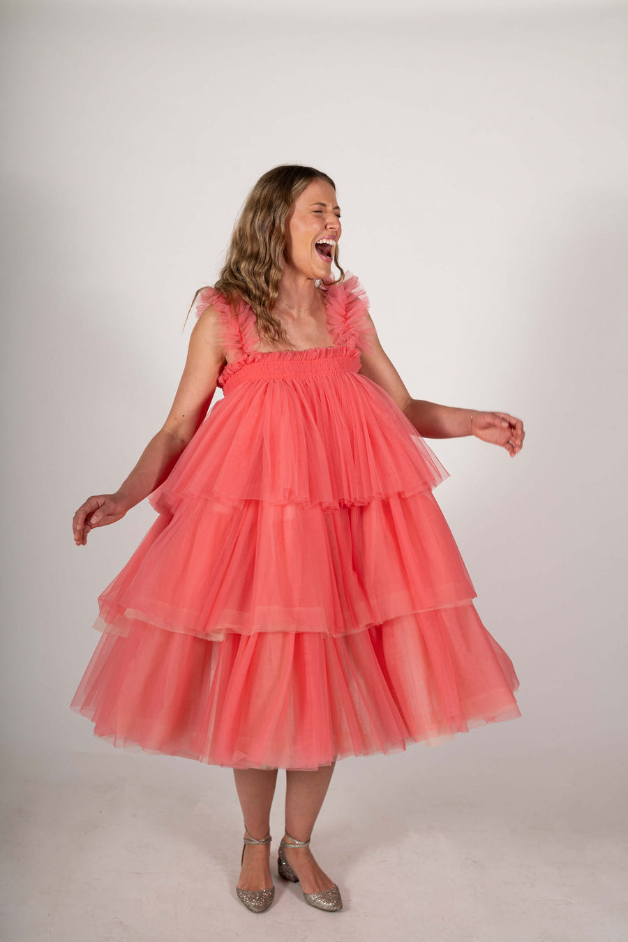 Model laughs while twirling in the Mariposa Tulle Midi dress in pink sorbet by House of Campbell.
